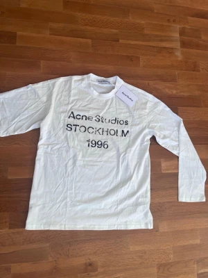 Vit långärmad tröja Acne Studios - Vit långärmad tröja från Acne Studios med tryck i svart text på bröstet: 'Acne Studios STOCKHOLM 1996'. Tröjan har rund hals och är gjord i mjuk bomull. Perfekt för en clean och stilren look.