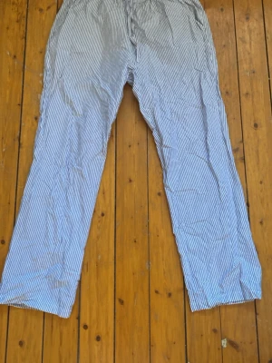 Randiga pyjamasbyxor i bomull - Säljer ett par klassiska pyjamasbyxor med tunna blå och vita ränder. Byxorna har rak passform och resår i midjan. Materialet känns lätt och luftigt, troligen bomull. Köpta på Lager157.