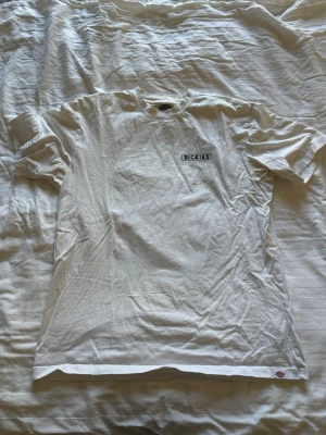 Vit Dickies t-shirt med tryck - Säljer en vit t-shirt från Dickies med liten logga på bröstet och stort färgglatt tryck på ryggen med texten 'Dickies Since 1922'. Klassisk passform och rund hals. Perfekt för dig som gillar streetwear och snygga prints.