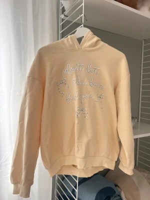 Gul hoodie med broderad text - Ljusgul hoodie med huva och broderad text på bröstet som säger 'don't let the bows fool you' tillsammans med små rosett-detaljer. Hoodien har en avslappnad passform och ribbade muddar vid ärmar och nederkant. Perfekt för en chill och trendig look.