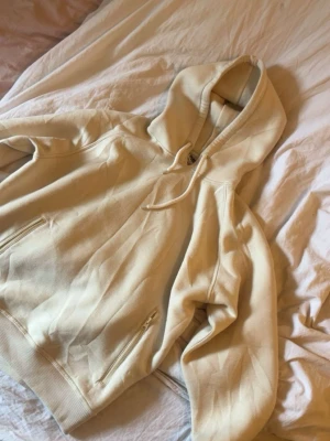 Beige hoodie med dragkedjefickor - Snygg beige hoodie med huva och dragsko. Hoodien har dragkedjefickor på sidorna och ribbade muddar vid ärmslut och nederkant. Perfekt för en avslappnad och trendig stil. Mjuk och skön bomullskänsla.