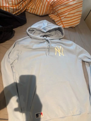 Ljusblå New York Yankees hoodie - Snygg ljusblå hoodie från New Era med New York Yankees-logga broderad i vitt på bröstet. Klassisk känguruficka framtill, dragsko i huvan och mjukt material som känns skönt mot huden. Perfekt för dig som gillar sportig streetstyle.