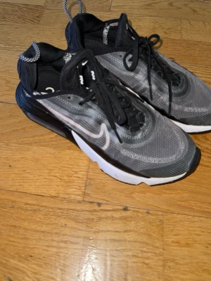 Nike Air Max 2090 svarta/grå sneakers - Nike Air Max 2090 sneakers i svart och grå mesh med vita detaljer och synlig Air Max-dämpning i sulan. Skorna har en futuristisk design, svarta skosnören och vit sula med svarta partier. Perfekta för dig som gillar streetwear och sportig stil. Skickas så fort som möjligt