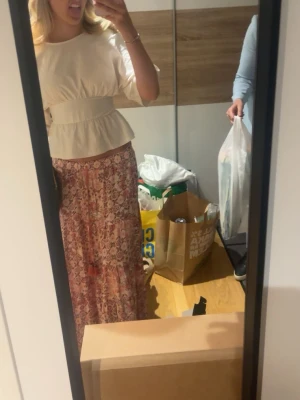 Lång blommig kjol i rosa toner - Säljer en lång, flowy kjol med blommigt mönster i rosa, lila och vita nyanser. Kjolen har en avslappnad passform och är perfekt för vår och sommar. Tillverkad i ett lätt och luftigt material som ger en skön känsla.