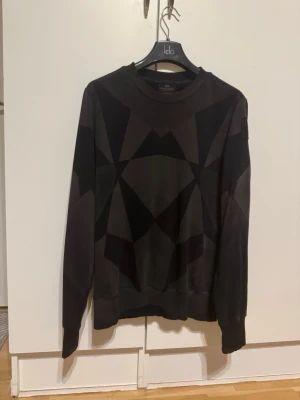 Parajumpers K2 Geomat Sweatshirt - Säljer en svart/grå sweatshirt från Parajumpers med geometriskt mönster. Tröjan har rund hals, långa ärmar och en patch med PJS-logga på ärmen. Tillverkad i mjukt bomullsmaterial för skön känsla. 85%Bomull, 15%Polyester