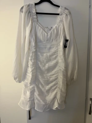 Vit klänning från Nly trend - Superfin vit kortklänning från Nly trend med långa puffärmar. Klänningen har v-ringning, rynkade detaljer och är tillverkad i ett lätt, luftigt material som ger en romantisk känsla.
