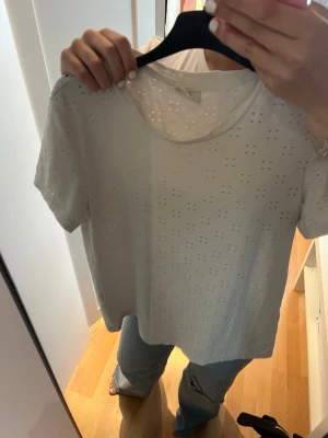 Vit broderad t-shirt med hålmönster - Säljer en vit t-shirt med korta ärmar och broderat hålmönster över hela plagget. T-shirten har en klassisk rund halsringning och är gjord i ett mjukt bomullsmaterial. Perfekt för dig som gillar en enkel men ändå unik stil.