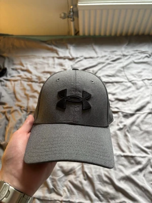 Mörkgrå keps från Under Armour - Snygg mörkgrå keps från Under Armour. Storleken är S/M, sitter ganska tajt.