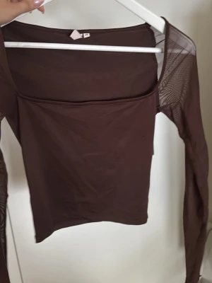 Brun mesh topp med lång ärm - Snygg brun mesh topp med lång ärm och fyrkantig urringning. Tunn och genomskinlig, perfekt för lager på lager eller som statement-plagg. Trendig och enkel att styla till olika looks.