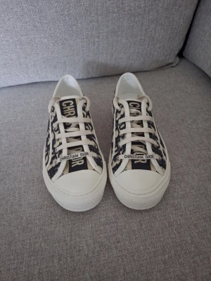 Dior Walk'n'Dior sneakers 37 - Snygga Dior Oblique sneakers i beige och marinblå canvas med klassiskt monogrammönster. Skorna har vita snören, gummisula och tydlig Christian Dior-logga på plösen. Perfekta för dig som vill ha en lyxig och trendig look.