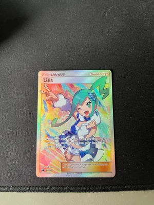 Pokémonkort Lisia Trainer Full Art - Säljer ett Pokémonkort av typen Trainer Supporter med Lisia-motiv. Kortet är en färgglad full art med holografisk yta och detaljer i blått, grönt och rosa. Perfekt för samlare eller Pokémon-fans som vill utöka sin kortsamling. Säljer även en Charizard ifrån xy evolutions (2016)