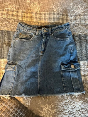 Jeanskjol med fickor från Bik Bok - Säljer en snygg blå jeanskjol från Bik Bok i klassisk denim med rå kant nertill och stora fickor med knapp på sidorna. Kjolen har normal passform💕 Kjolen är inte använd särskilt många gånger och är i bra skick🤗