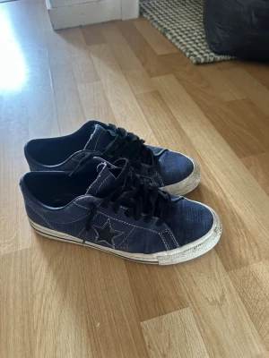 Mörkblå Converse One Star sneakers - Snygga mörkblå Converse One Star sneakers i denimliknande tyg med svart stjärndetalj på sidan. Skorna har vita sulor med svarta ränder och svarta skosnören. Perfekta för en avslappnad streetstyle-look. Smutsiga men bra skick