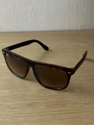 Bruna Ray-Ban solglasögon Wayfarer - Snygga solglasögon från Ray-Ban i klassisk Wayfarer-modell. Bågarna är bruna med en lätt transparent finish och glasen är mörktonade. Perfekta för dig som vill ha en tidlös och cool stil. Ray-Ban-loggan syns på linsen.