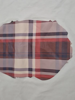 Vit t-shirt med rutig patch - Säljer en vit t-shirt från A Bathing Ape med en stor rutig patch i rött, blått och beige på framsidan. Klassisk passform och liten BAPE-logga på ärmen. Tillverkad i mjuk bomull, perfekt för en avslappnad streetwear-look.