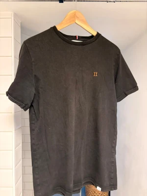 Svart t-shirt från Les Deux - Stilren, lite tightare svart t-shirt från Les Deux med diskret guldfärgad 'II'-logga på bröstet. .