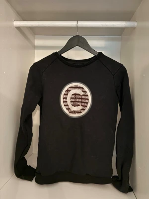 Svart sweatshirt från Colmar - Cool svart sweatshirt från Colmar med rund halsringning och ett stort tryckt Colmar Originals-märke på bröstet. Tröjan har långa ärmar och ribbade muddar vid ärmslut och nederkant. Perfekt för en avslappnad streetwear-look.