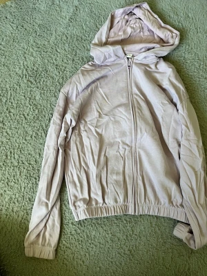 Ljuslila hoodie med dragkedja - En stilren ljuslila hoodie med dragkedja framtill och huva. Hoodien har långa ärmar, ribbade muddar och resår i nederkant. Perfekt för en avslappnad och chill look. Materialet känns mjukt och bekvämt mot huden.