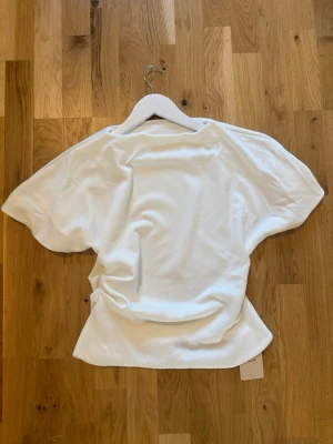 Vit kortärmad t-shirt i bomull - En basic vit t-shirt med korta ärmar och avslappnad passform. Tillverkad i mjuk bomull som känns skön mot huden. Perfekt att matcha med jeans eller shorts för en clean look. Figursydd asymmetrisk t shirt 