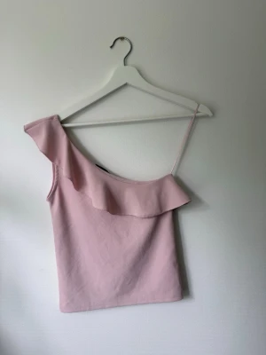 Rosa Topp - En rosa topp från Stradivarius. Sitter över ena axeln. Fin passform och fin rosa färg som passar bra till sommar outfits. 