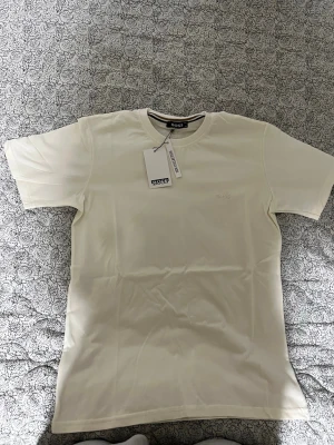 Vit kortärmad t-shirt - Snygg vit t-shirt med diskret broderad logga på bröstet. Klassisk rund halsringning och korta ärmar. Tillverkad i mjuk bomull för en skön känsla och stilren look. Perfekt basplagg till garderoben.