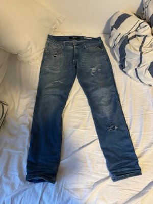 Blå slitna jeans från Replay - Säljer ett par blå jeans från Replay med slitningar. Riktigt schyssta och sitter skönt utan en för tight eller för Baggy passform