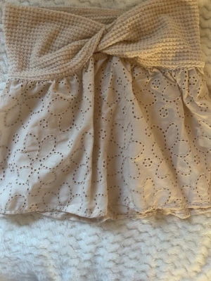  tubtopp - Söt beige tubtopp med virkad överdel och broderad spets i blommönster. Toppen är axelbandslös och har en twistad detalj framtill.  Aldrig använt. 