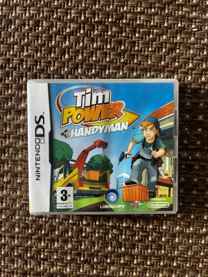 Tim Power Handyman Nintendo DS spel - Nintendo DS-spelet Tim Power Handyman från Ubisoft. Omslaget är färgglatt med tecknad stil och visar en hantverkare med verktyg och byggmaskiner. Spelet är licensierat av Nintendo och rekommenderas från 3 år.