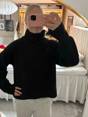 Svart polotröja i stickat material - Säljer en svart stickad polotröja med hög krage och långa ärmar. Tröjan har en rak passform och ribbade muddar vid ärmslut och nederkant. Perfekt för lager på lager och enkel att matcha med olika stilar🖤