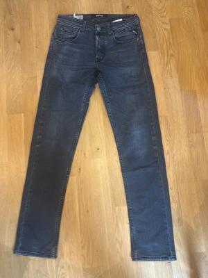 Grå slim fit jeans från Replay - Snygga grå slim fit jeans från Replay med klassisk femficksmodell och diskreta slitningar. Jeansen har normal midja, dragkedja och knappstängning samt Replay-logga på myntfickan. 