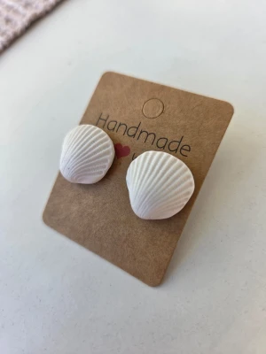 Handgjorda snäckformade örhängen - Säljer ett par handgjorda örhängen i form av vita snäckskal. Örhängena har en rundad, räfflad yta och lätt skimmer i sig. Stiften är av rostfritt stål. Gjorda för hand av mig i polymerlera. 