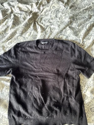 Svart stickad t-shirt Weekday - En svart stickad t-shirt från Weekday med rund halsringning och korta ärmar. Tröjan har en enkel och avslappnad passform, perfekt för en cool och minimalistisk stil. Materialet ser mjukt och lite luddigt ut.