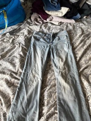Ljusblå bootcut jeans i bomull - Säljer ett par ljusblå bootcut jeans med klassisk femficksdesign och snygga detaljer på bakfickorna. Jeansen har normal passform och är tillverkade i mjuk bomull med en skön jeanskänsla. Perfekta för dig som gillar en avslappnad men trendig look.