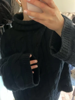 Svart supermysig tröja H&M - Svart kabelstickad polotröja från H&M med bred krage och långa ärmar. Tröjan har ett chunky och oversized fit med ribbade muddar vid ärmslut och nederkant. Perfekt för att hålla sig varm under kyliga dagar.