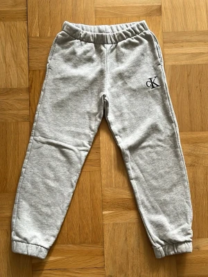 Gråa mjukisbyxor från Calvin Klein - Snygga gråa mjukisbyxor från Calvin Klein med broderad CK-logga framtill och en bakficka med Calvin Klein Jeans-etikett. Byxorna har resår i midja och benslut för skön passform. Perfekta för chill dagar eller när du vill vara bekväm. Storlek 8 år fundera inte släng bara iväg ett SMS vid vilken fråga som helst!☺️📦📩