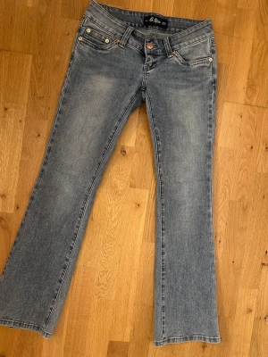 Blå bootcut jeans från G Rise Jeans - Säljer ett par klassiska blå bootcut jeans från G Rise Jeans med fem fickor och snygga kopparfärgade knappar. Jeansen har låg midja och en lätt tvättad look som ger en avslappnad vibe. Perfekta till sneakers eller boots!