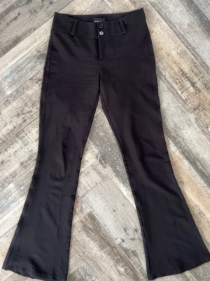 Svarta bootcut kostymbyxor - Säljer ett par svarta kostymbyxor med bootcut passform och medelhög midja. Byxorna har två knappar framtill, bälteshällor och fickor med lock bak. Perfekta för en trendig och stilren look. Materialet är mjukt och i följsam blandning, troligen polyester eller viskos. Pris kan diskuteras!  Hör av er vid funderingar!😊