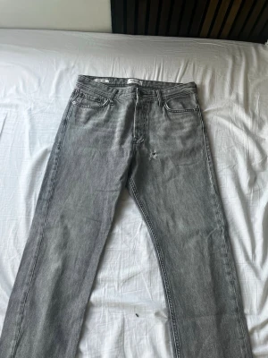 Grå raka jeans från Jack&jones - Säljer ett par grå raka jeans från jack&jones med klassisk femficksmodell och knappgylf. Jeansen har en avslappnad passform och är tillverkade i slitstark denim. Perfekta för en casual look och funkar året runt.
