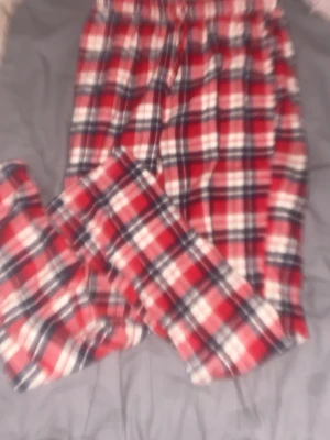 Rödrutiga pyjamasbyxor i flanell - Mysiga pyjamasbyxor i mjuk flanell med klassiskt rött, vitt och mörkblått rutmönster. Byxorna har resår i midjan och dragsko för extra komfort. Perfekta för slappa dagar hemma eller sköna nätter.