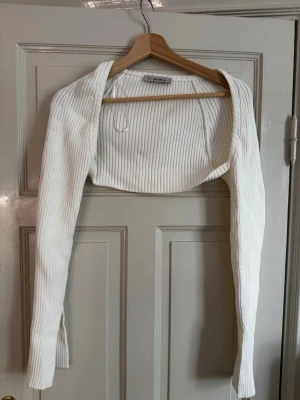 Vit ribbad bolero från Dilvin knit - Säljer en vit ribbad bolero från Dilvin knit. Den har lång ärm, croppad passform och är tillverkad i ett stretchigt, mjukt material. Perfekt att slänga över ett linne eller klänning för en trendig lager-på-lager-look. Använd några gånger men i ett bra skick.💕