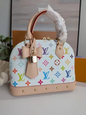 Iouis Vuitton BB Murakami Edition 🪷 - En dröm i färg och form Denna ljuvliga handväska utstrålar en tidlös charm med sin mjuka, kupolformade silhuett som påminner om klassisk elegans. Den står stadigt på en vacker bas, redo att bära dina mest värdefulla ägodelar genom livets alla små och stora ögonblick.Väskan omfamnas av två handtag i naturligt, ljusbeige läder som med tiden kommer att bära spår av dina resor och äventyr.