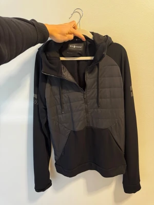 Sail Racing  - Snygg svart hoodie från Sail Tacing med dragkedja framtill och quiltad panel på bröstet. Köpt från Johnells…