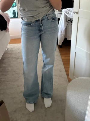 Ljusblå vida jeans - Säljer ett par ljusblå vida jeans med medelhög midja och klassisk femficksdesign. Jeansen har en avslappnad passform över låren och lätt utsvängda ben. Perfekta till sneakers eller boots och ger en snygg retrovibe till din outfit.