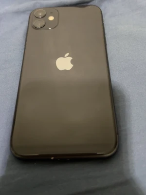 Svart iPhone 11 med 64gb utrymme, Batteri kapacitet ligger på 100% (utbytt från en tekniker inte originala) - Snygg svart iPhone 11 med rundade kanter och glasbaksida. Telefonen har två kameror på baksidan och den klassiska Apple-loggan i silver. Perfekt för dig som gillar stilren design och vill ha en mobil som känns modern i handen.