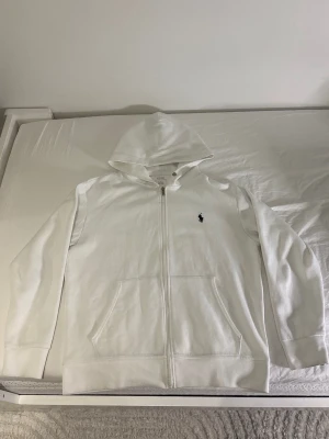 Vit hoodie från Polo Ralph Lauren - Snygg vit hoodie med dragkedja från Polo Ralph Lauren. Klassisk design med huva, två stora fickor framtill. Tillverkad i mjukt bomullsmaterial. Kom gärna med prisförslag eller frågor.