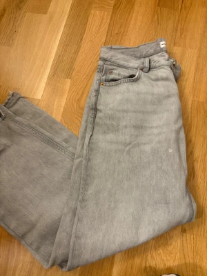 Grå raka jeans med rå kant - Säljer ett par grå jeans med rak passform och rå, fransig kant nedtill. Jeansen har klassisk femficksdesign och är tillverkade i bomull. Perfekta för en avslappnad och trendig look.