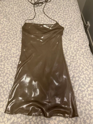 Silver klänning Gina Tricot - Säljer en glansig silverfärgad kort klänning från Gina Tricot. Klänningen har tunna axelband och en figurnära passform med snygg glansig finish. Knyts i nacken, använd en gång!