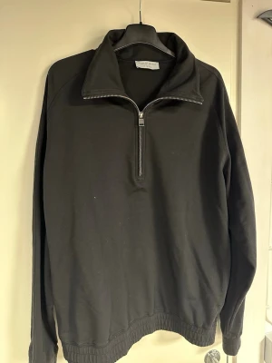 Svart half-zip hoodie Tiger of Sweden - Snygg svart hoodie från Tiger of Sweden med halv dragkedja framtill och hög krage. Tillverkad i mjukt bomullsmaterial. Storlek M