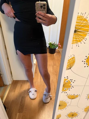 Svart tight minikjol - Säljer en svart tight minikjol med slits på sidan. Kjolen har en enkel och stilren design, perfekt för att matcha med olika toppar. Materialet känns mjukt och stretchigt för en bekväm passform.