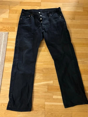 Svarta Levi's raka jeans herr - Säljer ett par svarta Levi's jeans med rak passform och klassisk femficksdesign. Jeansen har knappgylf. Perfekta för dig som gillar en tidlös och enkel stil.